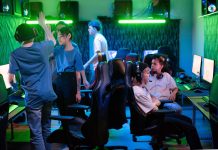 PGL Masters Bucharest 2026 Preview: Teams, Format, and Schedule Gamers interacting at a gaming lounge, with one player raising a hand for a high-five as others sit at their gaming PCs under neon green and blue lighting.